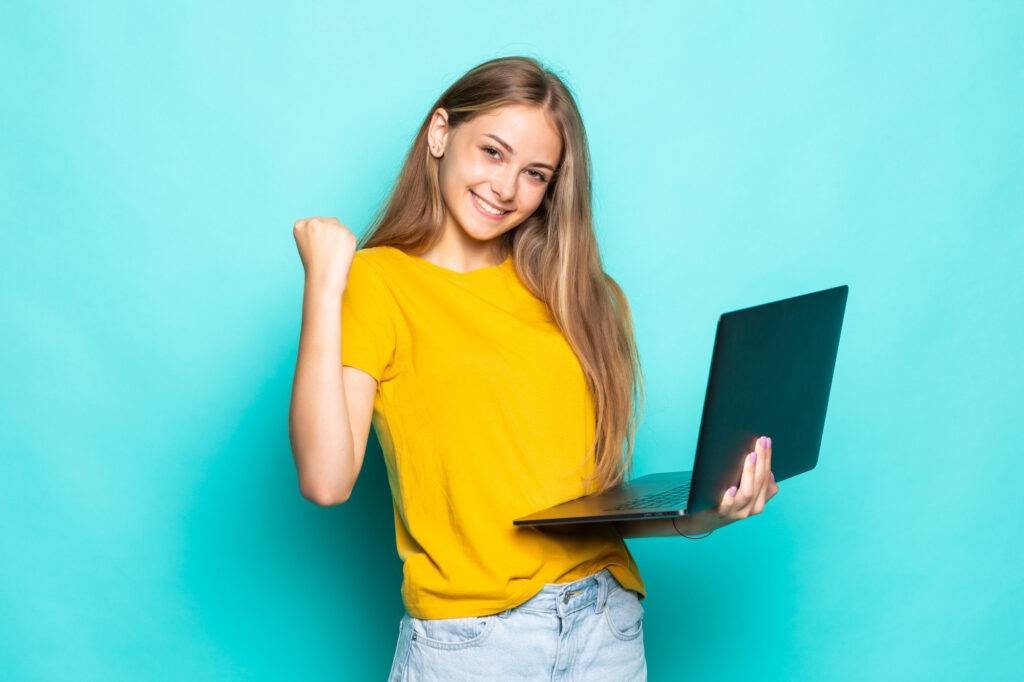 young woman working laptop with win gesture posing isolated turquoise wall